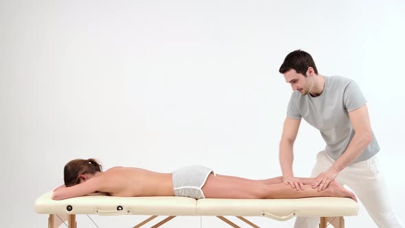 Male masseur with strong hands massaging lower part of leg to young woman lying on massage table alt