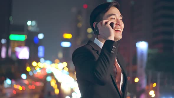 Asian young business man standing with happiness outdoor using mobile phone downtown in city. alt