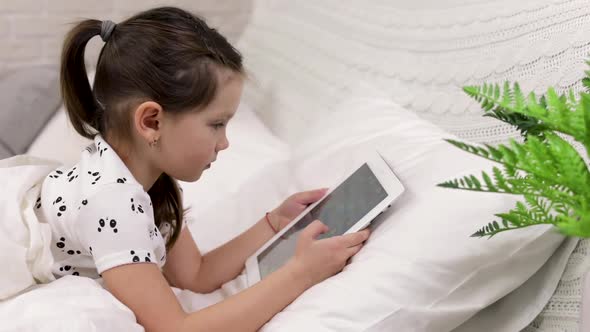 Cute Little Child Girl Lies in Bed Uses Digital Tablet