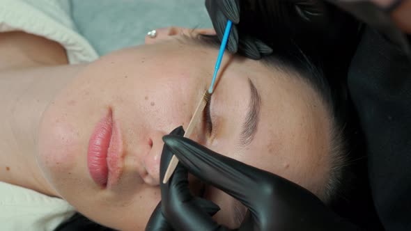 Master in Eyelash Extension with a Small Brush Combs the Client's Eyelashes alt