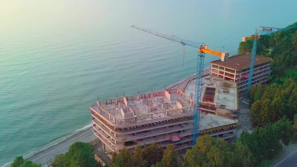 crane is working on construction site view from a drone on background of sea.