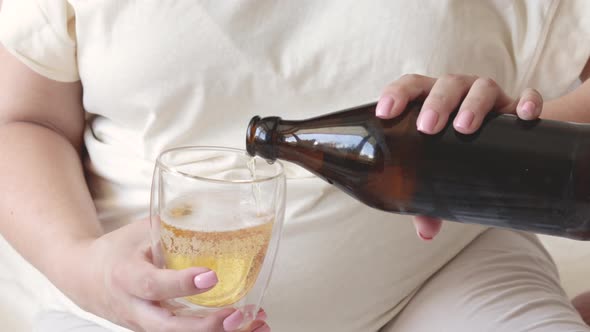 pregnant woman pour beer from bottle to glass.big advanced belly in background.third trimester.