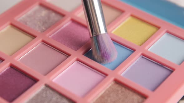 Make-up artist picks up blue pigment from bright colorful eyeshadow palette with a brush. alt