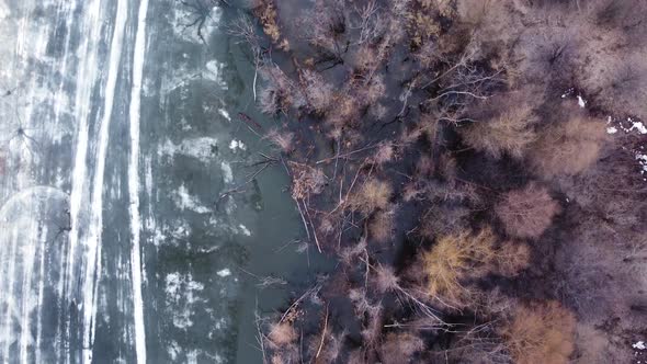 Aerial top down view of the shore of a lake with thin melted ice on the surface of the water.