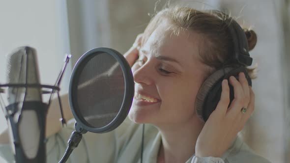 A Young Girl Emotionally Sings Into a Microphone in the Background of the Window alt