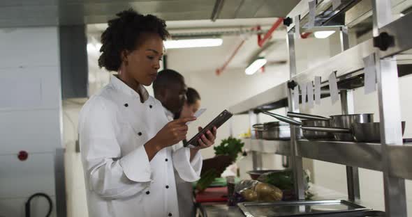 African american female chef taking orders and using tablet in restaurant kitchen alt