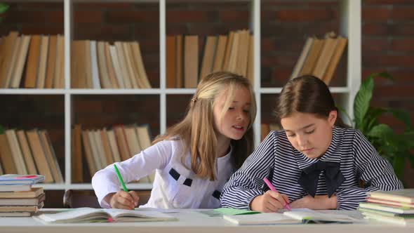 Portrait of young schoolgirls sitting at table desk at library or home doing homework