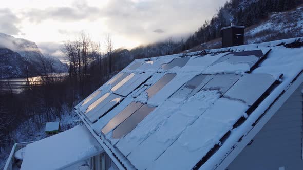 Solar panels on private home covered in snow - Smoke from chimney with stunning fjord landscape back alt