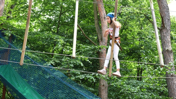 Little happy child girl in adventure park in safety equipment in summer day. Happy childhood concept alt