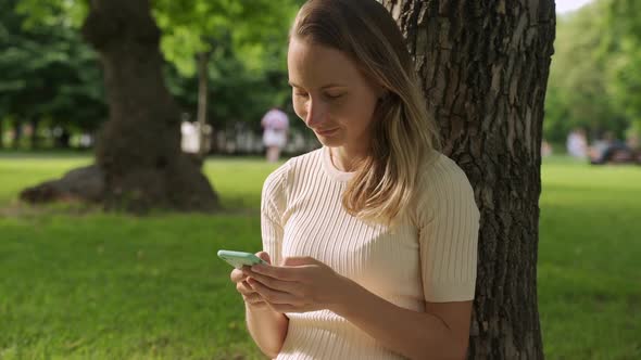Close Up of a Beautiful Young Woman, That Is Using an Application in Her Smart Phone in Park alt