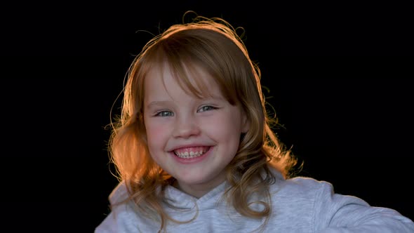 Close up portrait of cheerful little girl on dark studio background