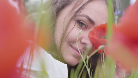 Portrait of Cute Young Woman Sitting in Poppy Field Looking at Camera. Connection with Nature. Green alt