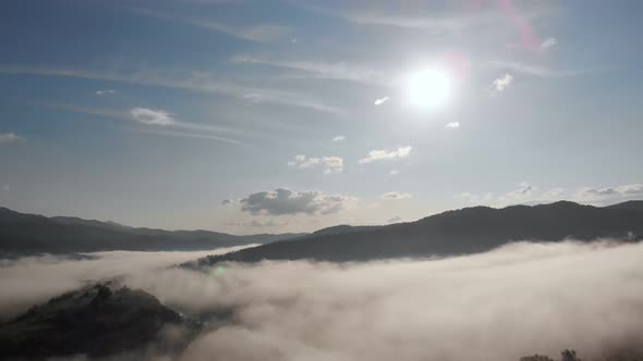 Aerial Drone Flight View Over Low Clouds and Morning Mist Covered Mountain Slopes at Sunrise