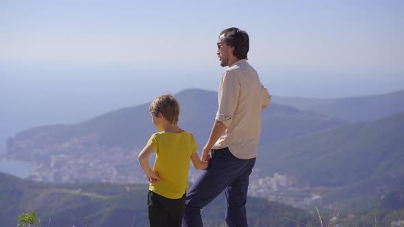 A Father and Son Standing on a View Point on a Mountain Look at the City of Budva alt