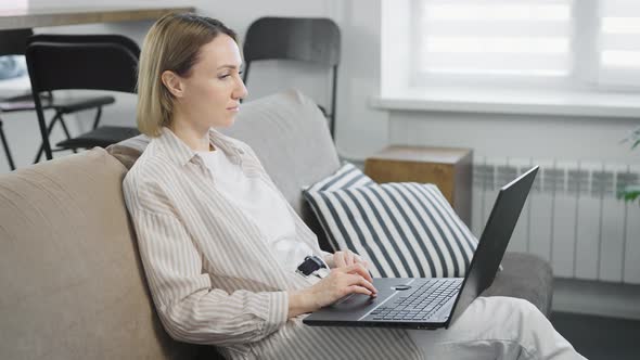 Pleasant Young Woman in Her Apartment Using a Modern Laptop for Work Online Shopping and alt