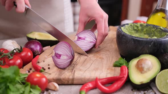 Making Guacamole Sauce  Woman Slicing Red Mars Onion in a Half on a Wooden Cutting Board alt