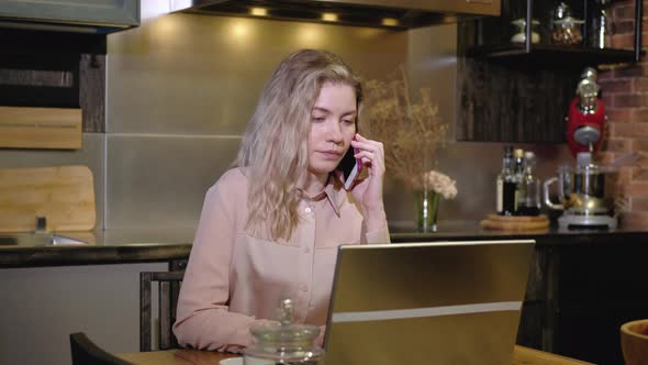 Girl in  kitchen on the phone is discussing an order with a client on a laptop alt