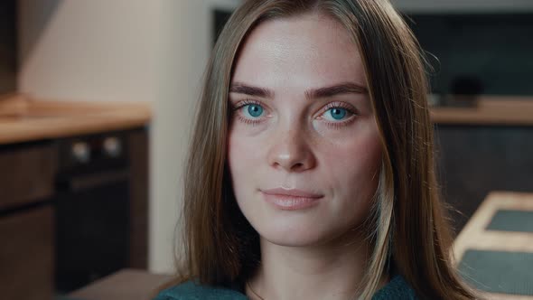 Close-up Portrait of Pretty Young Woman with Beautiful Blue Eyes Looking at Camera Sit on Sofa Alone alt