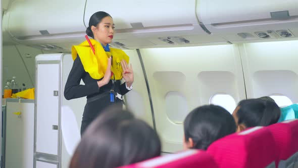 Asian flight attendant explaining and show safety demonstration on airplane before take off. alt
