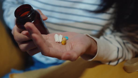 Sick asian young lady holding pill take medicine sit on couch in living room at home night.