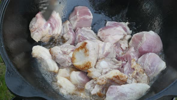 Cooking Process, Frying Pork Meat and Onion in Large Cauldron on Open Fire.  Man Cooking Meat