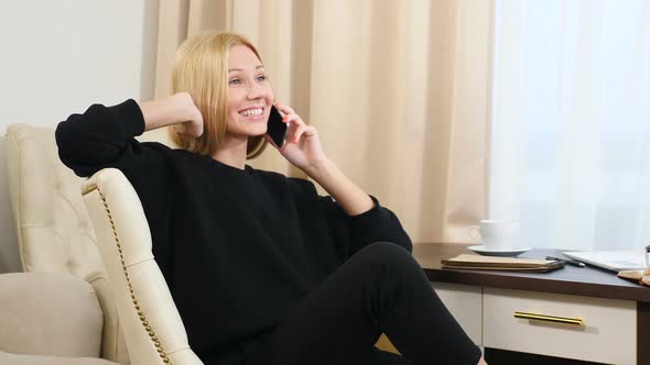 Happy Successful Woman in Bright Apartment Using Mobile Phone Sitting Comfortably alt