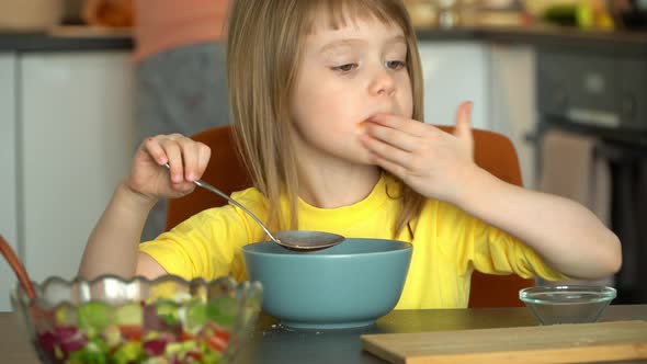 Little Girl Eats Tomato Soup with Croutons and Cheese on Kitchen