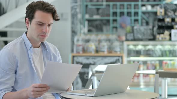 Young Man with Laptop Having Loss on Documents alt