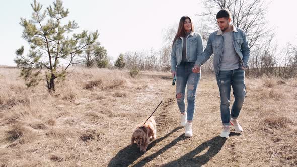 Young Man and Woman in Denim Are Walking in the Wheat Field with a Dog alt
