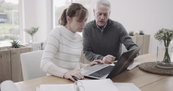 Senior couple doing domestic finance on laptop at kitchen table, day in life