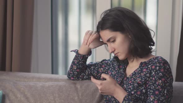 Portrait of a Pretty Brunette Girl with a Phone in Her Hands Uses a Mobile App alt