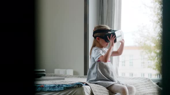 Little Girl in VR Goggles Sitting on Bed and Watching Video