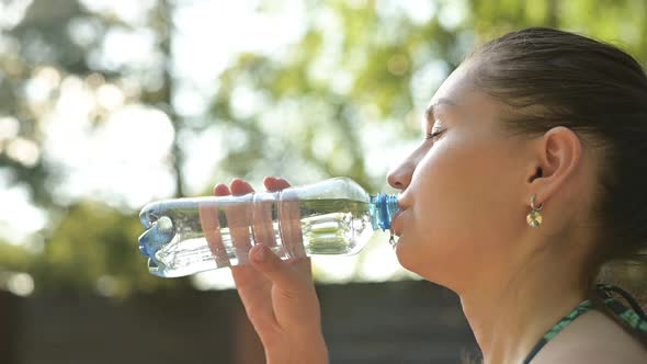 Young woman delightfully drinks water from a bottle on a hot summer day alt
