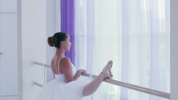 Young Graceful Ballerina is Stretching Tilting to Her Leg Near the Barre Stand