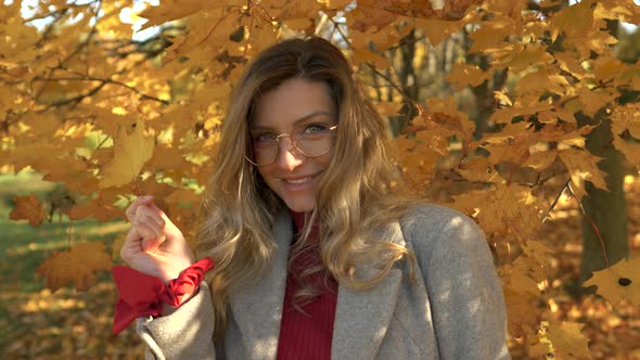 blond woman smiles and plays with yellow and golden leaf in autumn park alt