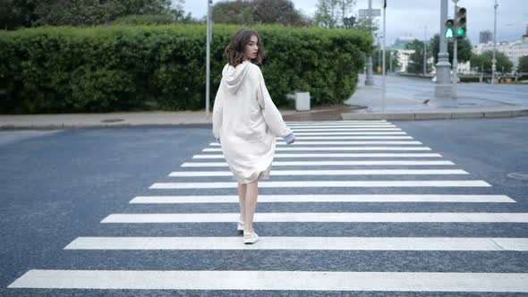 A Girl at a Pedestrian Crossing Turns on Camera Cityscape on the Background