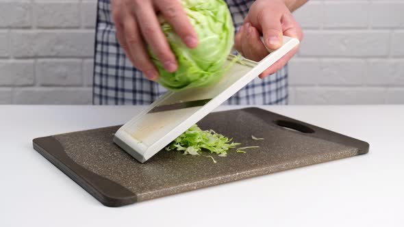 Male hand chopping greeen cabbage for a salad with a grater.