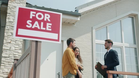 Real Estate Agent in Suit Talking to Couple of Buyers Showing New Suburban House alt