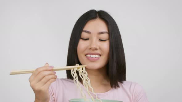 Asian Woman Holding Noodles With Chopsticks Posing Over White Background alt
