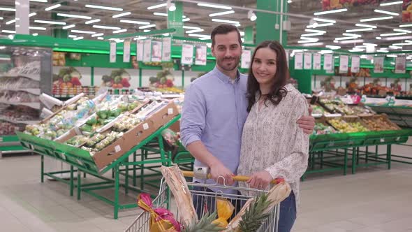 Attractive happy millennial couple shopping in supermarket with shopping cart