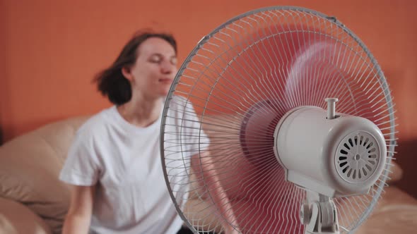 Young Woman Sits in Front of Electric Home Fan Air Stream Blowing Short Hair alt