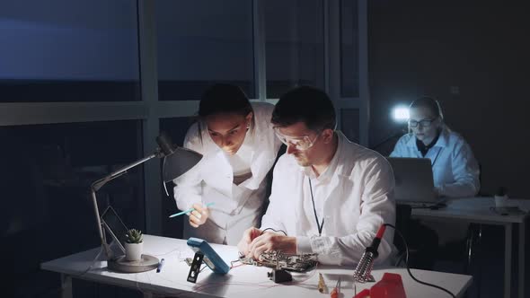 Mixed Race Electronics Engineers in White Coats Working on Motherboard Using Multimeter Tester alt