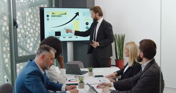 Bearded Team Leader Holding a Presentation on Digital Whiteboard in Meeting Room alt
