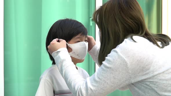Asian Mother Puts A Safety Mask On Her Son Face alt