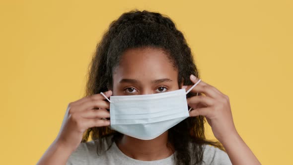 Studio Portrait of Cute African American Girl Teenager Putting on Protective Medical Mask and alt