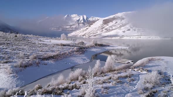 Flying through white frozen trees in winter landscape next to lake alt