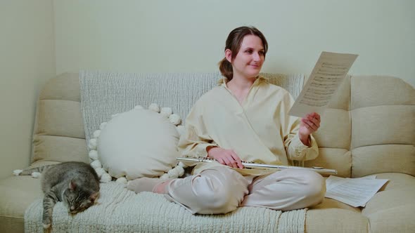 Woman musician with flute looks at notes on sofa in living room