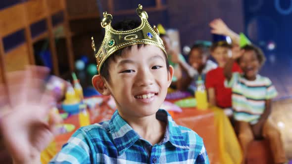 Boy in crown waving his hand during birthday party alt