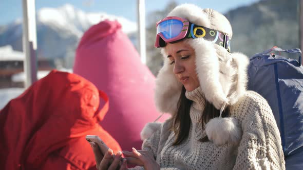 Happy Woman in Ski Resort Sitting in the Cafe and Texting with Her Friends in the Social Network