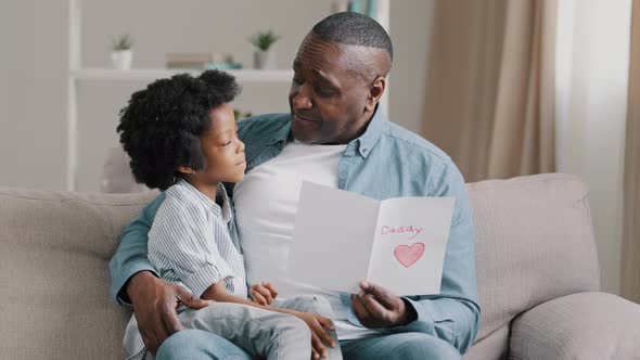 Happy Man Sitting on Couch Hugging Beloved Daughter Reading Postcard Cute Kid Girl Wishes Dad Happy alt